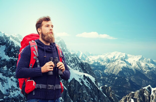 concepto de aventura, viajes, turismo, caminatas y personas - hombre con mochila roja y binocular sobre fondo de montañas alpinas