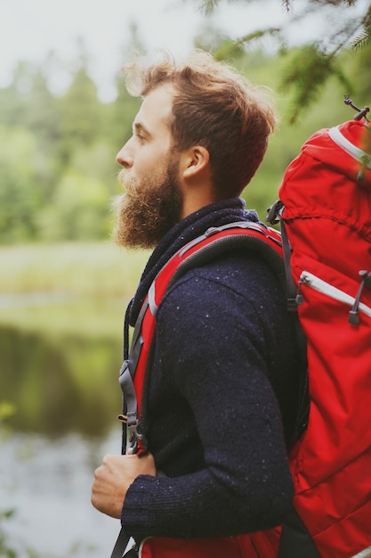 concepto de aventura, viajes, turismo, caminatas y personas - hombre sonriente con barba y mochila roja caminando