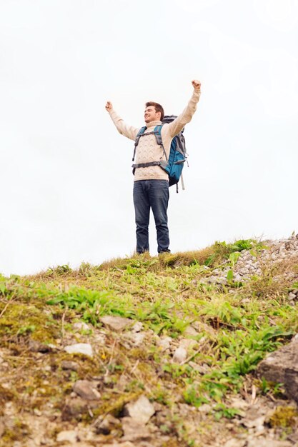 concepto de aventura, viajes, turismo, caminatas y personas - hombre sonriente con mochila levantando las manos al aire libre