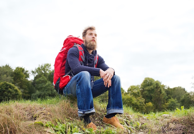 concepto de aventura, viajes, turismo, caminatas y personas - hombre sonriente con mochila roja sentado en el suelo