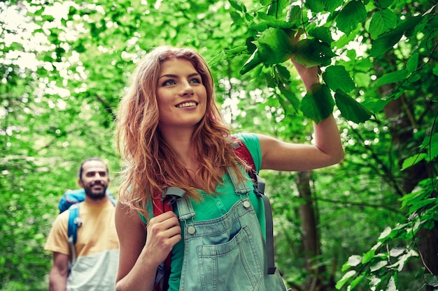 concepto de aventura, viajes, turismo, caminatas y personas - pareja feliz caminando con mochilas en el bosque