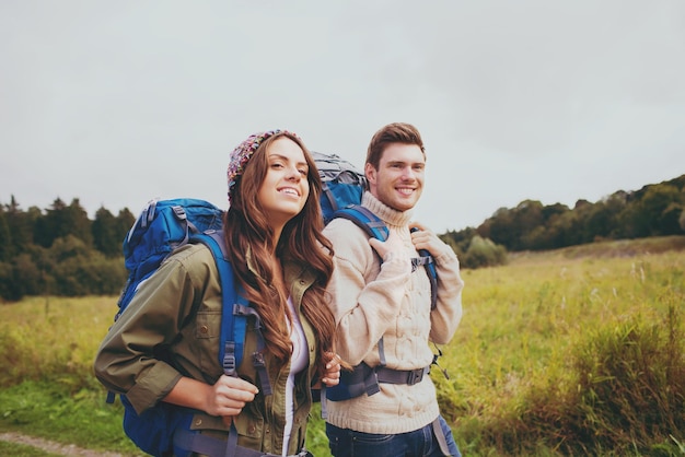 concepto de aventura, viajes, turismo, caminatas y personas - pareja sonriente caminando con mochilas al aire libre