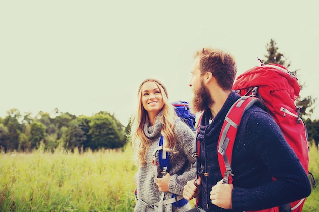 concepto de aventura, viajes, turismo, caminatas y personas - pareja sonriente caminando con mochilas al aire libre