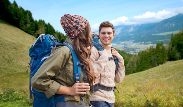 concepto de aventura, viajes, turismo, caminatas y personas - pareja sonriente caminando con mochilas sobre el fondo de las colinas alpinas