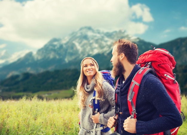 concepto de aventura, viajes, turismo, caminatas y personas - pareja sonriente caminando con mochilas sobre el fondo de las montañas alpinas