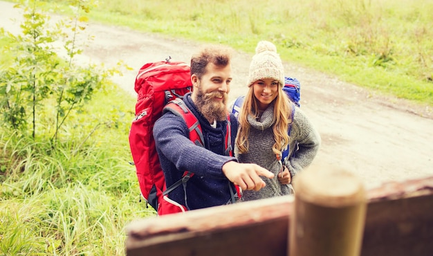 concepto de aventura, viajes, turismo, caminatas y personas - pareja sonriente con mochilas de pie en el cartel al aire libre