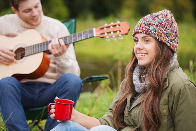 concepto de aventura, viajes, turismo y personas - pareja sonriente con guitarra en camping