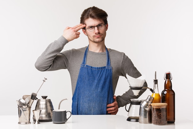 Concepto de barista, trabajador de café y barman. Empleado molesto con el cliente, el extraño mal gusto en el café hace que el suicida firme con la pistola cerca de la cabeza, de pie sobre la barra del bar en el delantal,