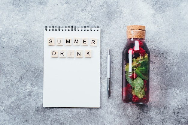 Concepto de bebida de verano Berry limonada en botella de vidrio con cuaderno en blanco blanco y letras de madera