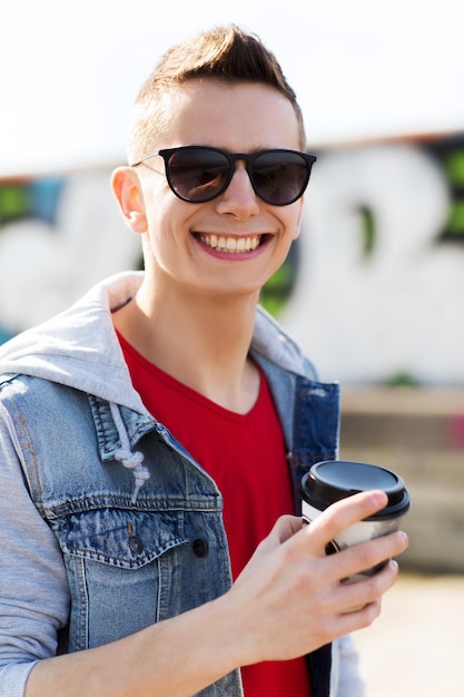 concepto de bebidas y personas - joven sonriente o adolescente bebiendo café de una taza de papel al aire libre