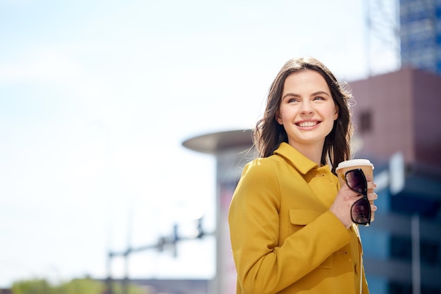 concepto de bebidas y personas - mujer joven feliz o adolescente bebiendo café de un vaso de papel en la calle de la ciudad