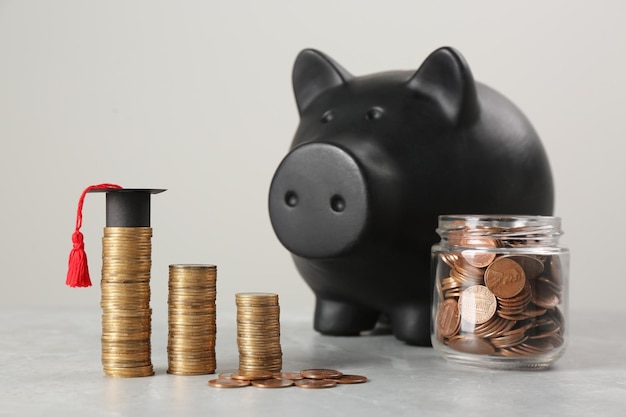 Concepto de beca Tapa de graduación de hucha y monedas en mesa gris claro