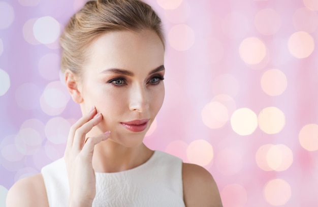 concepto de belleza, boda y gente - hermosa mujer sonriente con vestido blanco tocando su cara sobre cuarzo rosa y fondo de luces de serenidad