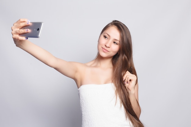 Concepto de belleza, cuidado de la piel y personas - Spa Woman. Hermosa chica después del baño tocando su rostro. Piel perfecta. Protección de la piel. Hora de hacerse un selfie. Mujer joven feliz tomando selfie. Mimos. Tratamiento