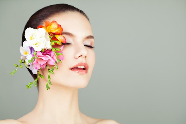 Concepto de belleza y cuidado de la piel Spa Mujer joven con piel sana y flores brillantes sobre fondo gris con espacio de copia