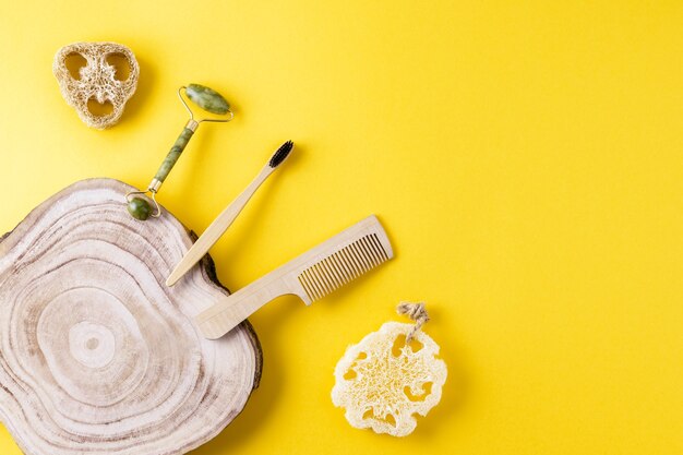 Concepto de belleza ecológica. Rodillo de cara de jade, esponjas de lufa, cepillo de dientes, peine de madera, rebanada de madera sobre superficie amarilla. Conjunto de artículos de belleza a partir de material ecológico. Cero residuos para el baño. Copie el espacio, endecha plana