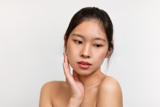 Concepto de belleza esencial joven china tocando su piel suave mujer asiática posando sobre blanco