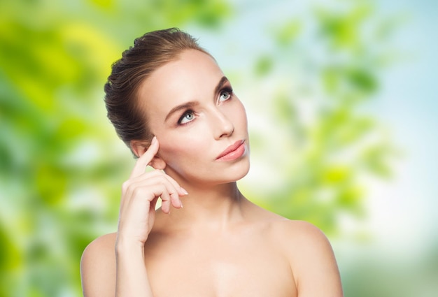 concepto de belleza, gente, eco y salud - hermosa mujer joven tocando su cara sobre fondo natural verde