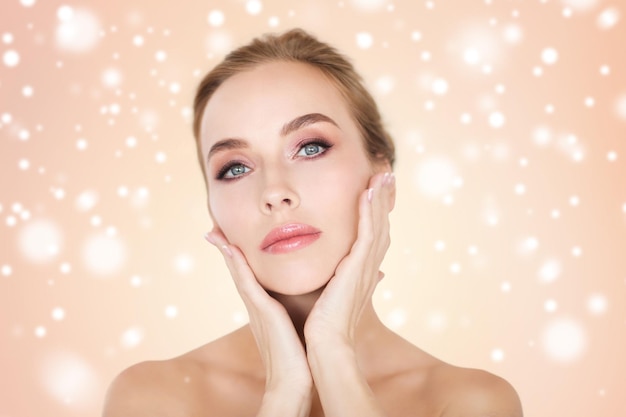 concepto de belleza, gente, invierno y cuidado del cuerpo -hermosa cara de mujer joven y manos sobre fondo beige y nieve