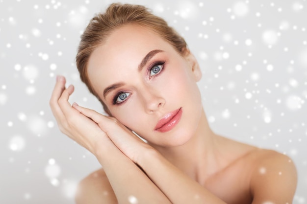 concepto de belleza, gente, invierno y cuidado del cuerpo - hermosa cara de mujer joven y manos sobre fondo gris y nieve