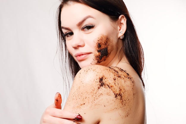 Foto concepto de belleza, gente y piel sana - mujer morena limpia la piel del cuerpo con exfoliación de café con fondo blanco aislado. retrato de belleza. hermosa mujer de spa tocando su rostro. piel fresca perfecta.