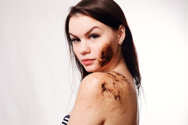 Concepto de belleza, gente y piel sana - Mujer morena limpia la piel del cuerpo con exfoliación de café con fondo blanco aislado. Retrato de belleza. Hermosa mujer de spa tocando su rostro. Piel fresca perfecta.