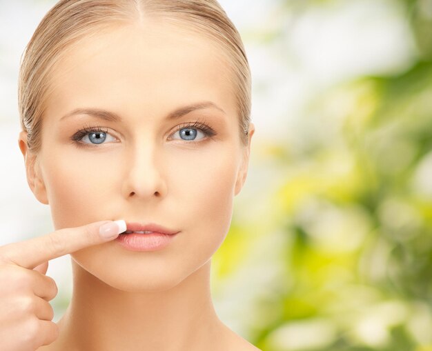 concepto de belleza, gente y salud - bella joven señalando con el dedo a sus labios sobre fondo verde