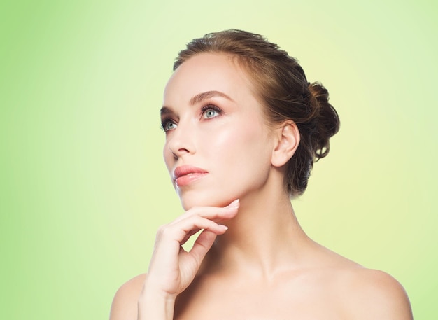 concepto de belleza, gente y salud - bella joven tocándose la cara sobre fondo verde