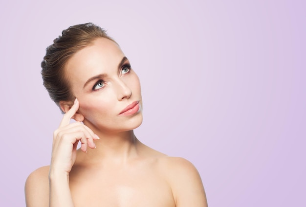 concepto de belleza, gente y salud - bella joven tocándose la cara sobre fondo violeta