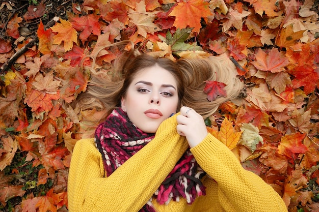 Concepto de belleza, gente, temporada y salud - chica guapa está acostada en hojas de otoño rojas amarillas