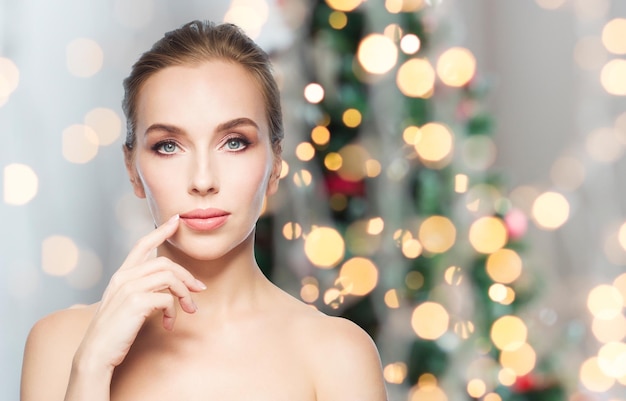 concepto de belleza, gente, vacaciones y cirugía plástica - hermosa mujer joven mostrando sus labios sobre el fondo de las luces del árbol de Navidad