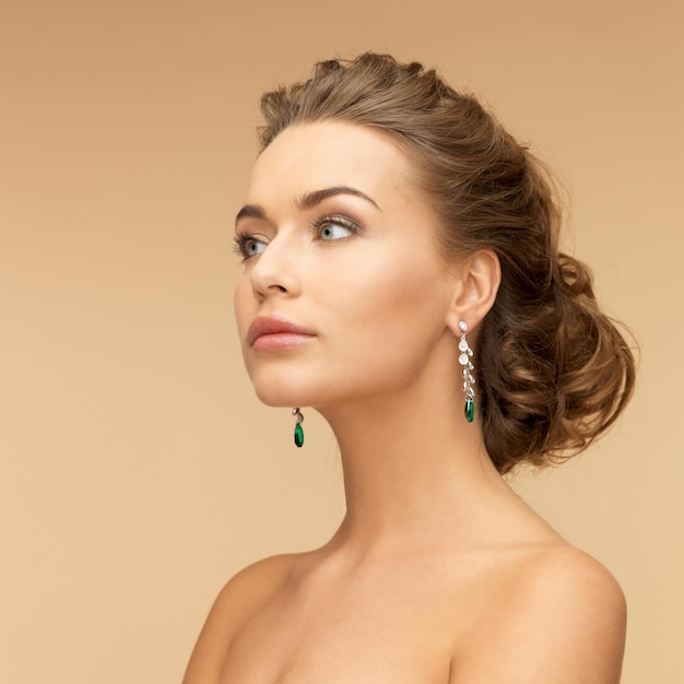 concepto de belleza y joyería - bella mujer con aretes de diamantes y esmeraldas