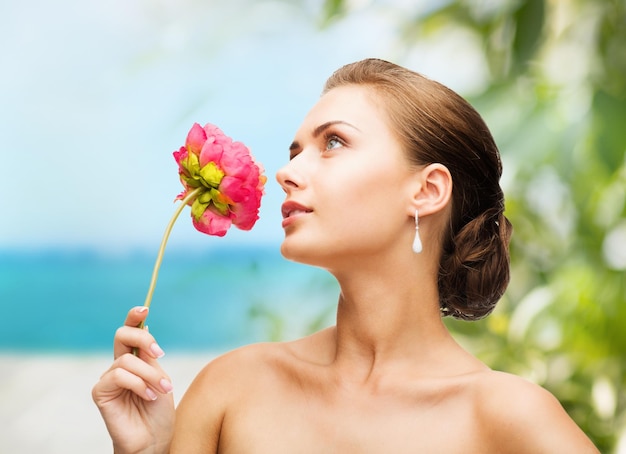 Concepto de belleza y joyería - mujer con aretes y oliendo flores