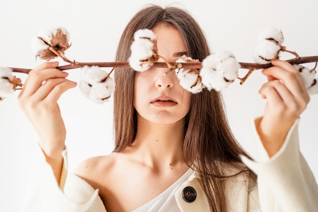 Concepto de belleza y juventud. Hermosa mujer en ropa acogedora con rama de flores de algodón