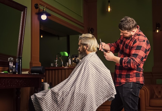 Concepto de belleza masculina afeitado Estilista en barbería hombre en peluquería con corte de pelo hipster barba y bigotes Estilista profesional en el interior de la barbería Retrato de hombre elegante barba