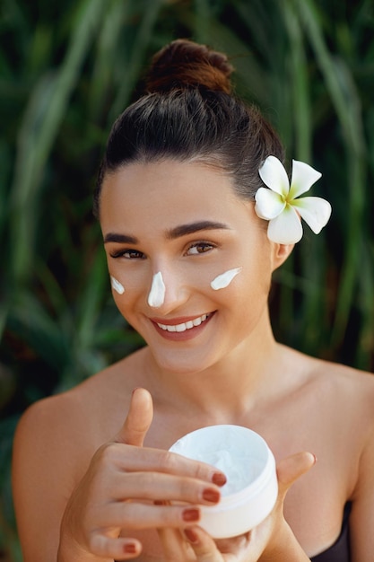 Concepto de belleza Mujer aplicando crema cosmética y mujer sonriente sostiene una botella de crema en la mano