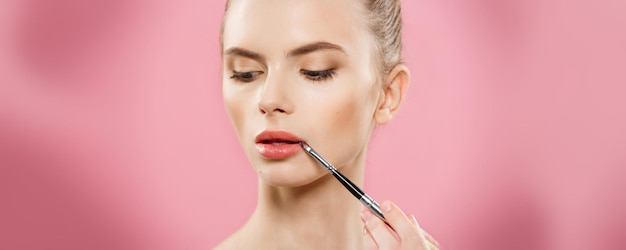 Concepto de belleza Mujer aplicando lápiz labial rojo con fondo de estudio rosa Hermosa chica hace maquillaje