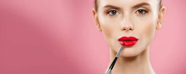 Concepto de belleza Mujer aplicando lápiz labial rojo con fondo de estudio rosa Hermosa chica hace maquillaje