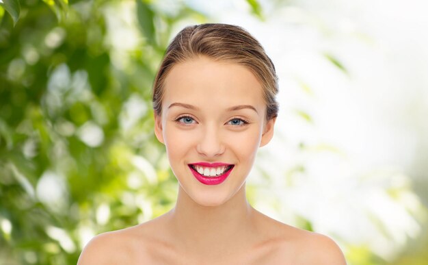 concepto de belleza, personas y salud - cara de mujer joven sonriente con lápiz labial rosa en los labios y hombros sobre fondo natural verde