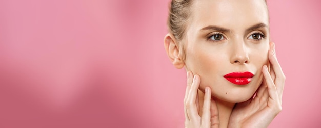 Concepto de belleza Primer plano Retrato de cara de mujer morena joven hermosa Modelo de belleza Chica con cejas brillantes maquillaje perfecto labios rojos tocando su rostro Aislado sobre fondo rosa