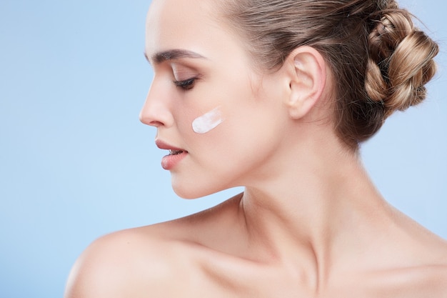 Concepto de belleza, retrato de belleza de mujer joven con crema en la mejilla. Perfil de mujer naturalmente hermosa mirando hacia abajo. Crema en la mejilla, cosmetología.