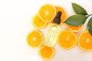 Foto concepto de belleza de suero de vitamina c en botella cosmética con cuentagotas y rodajas de fruta naranja sobre fondo blanco.