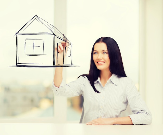 concepto de bienes raíces, alojamiento y tecnología - mujer sonriente dibujando casa en pantalla virtual