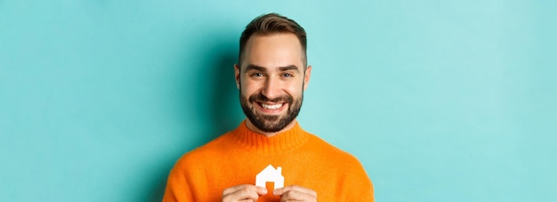 Foto concepto de bienes raíces joven feliz en busca de alquiler de casa sosteniendo casa papel maket y persona sonriente