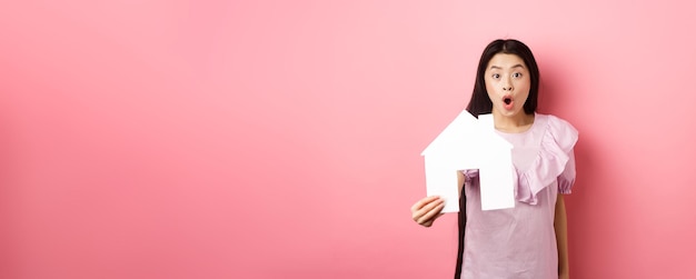 Foto el concepto de bienes raíces y seguros emocionó a la mujer asiática que muestra el recorte de la casa de papel y se ve asombrado spe