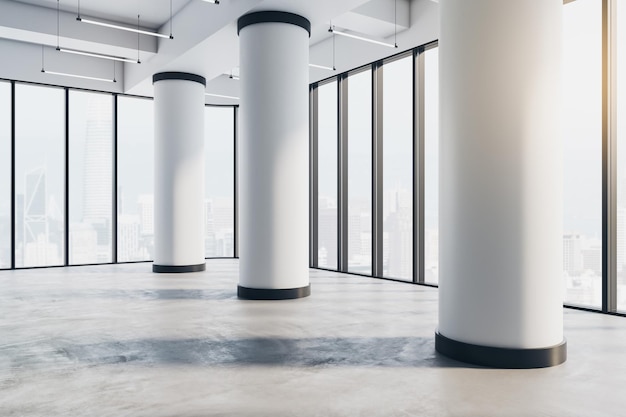 Concepto de bienes raíces con vista en perspectiva sobre enormes columnas blancas en el piso de concreto en un espacioso salón vacío con vista a la ciudad desde paredes de vidrio separadas por marcos negros 3D