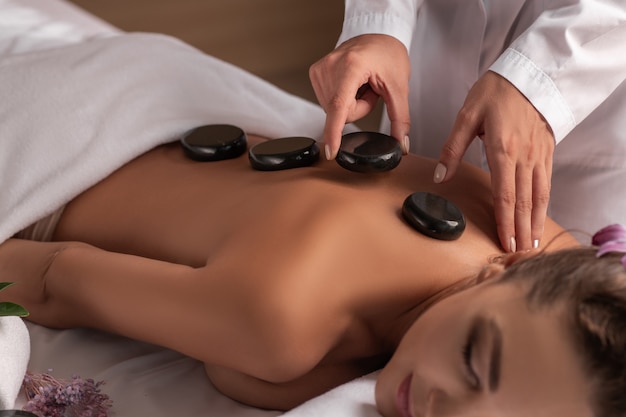 Concepto de bienestar, belleza y relajación - hermosa joven con masaje de piedras calientes en el spa