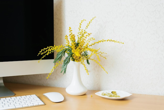 Concepto de un blogger independiente de negocios La computadora portátil está sobre una mesa de madera contra una pared blanca con una mimosa en un jarrón