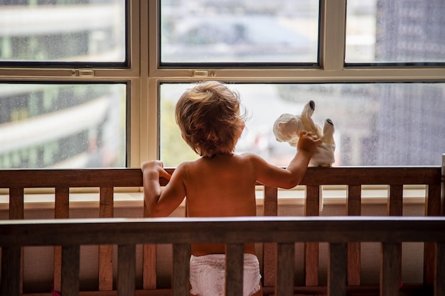 Concepto de bloqueo un niño pequeño en una cuna mira por la ventana en una calle de la metrópoli