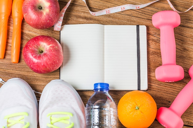 Concepto, botella de agua, mancuernas, zapatos deportivos, smartphone con auriculares y manzanas sobre fondo de madera. Espacio de la copia para el texto. Vista superior